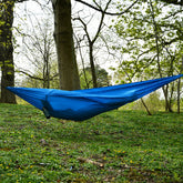 DD Chill Out Hammock set up in a green outdoor space surrounded by trees, perfect for relaxation.